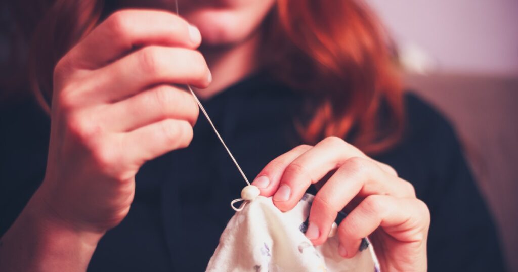 A red-haired woman pulling a threaded needle through a stitch as she repairs a shirt button.