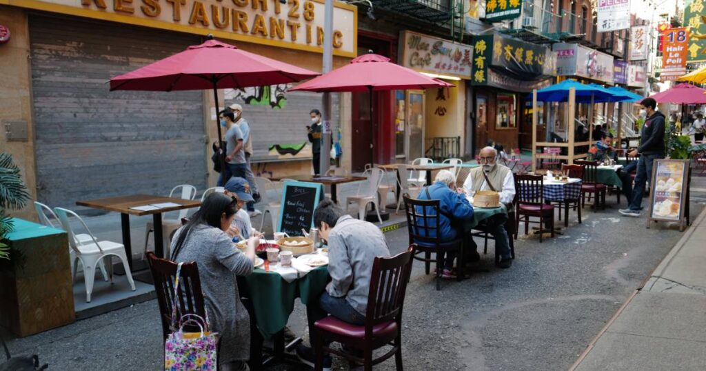 A downtown alleyway with tables and chairs set up for dining at a New York City dining hot spot. Guests are seated and eating.