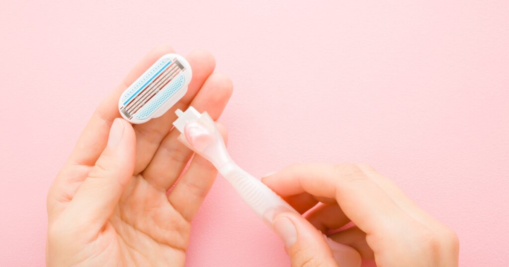A person is changing the razor blade head on a reusable razor. The handle of the razor is light pink.