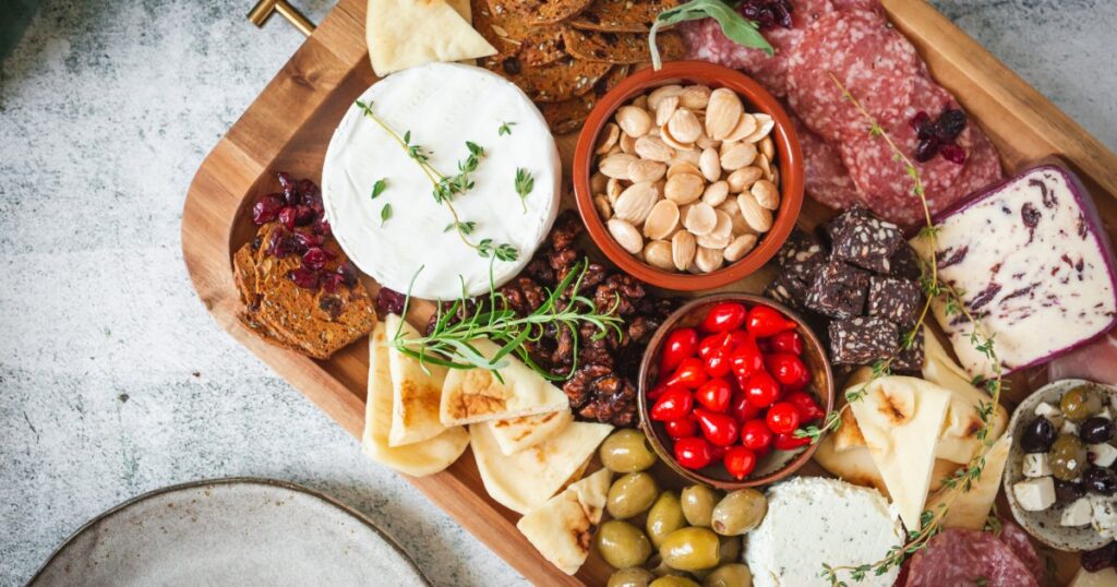 A charcuterie board with a wide selection of meats, cheeses, fruits, and mixed dry goods. The serving board is wood.