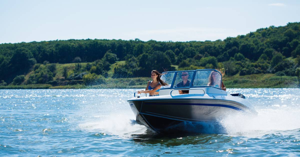 A woman wearing a bathing suit sits at the front end of a moving boat while a man drives and another woman sits beside him.