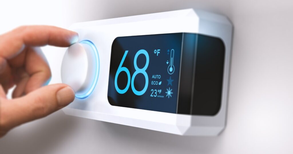 Close-up on an electronic digital display thermostat with a person's had adjusting the temperature setting.