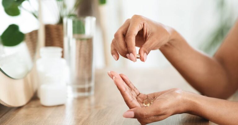 A woman's hand holds several gold yet transparent vitamins. She picks one out and holds it between her thumb and finger.