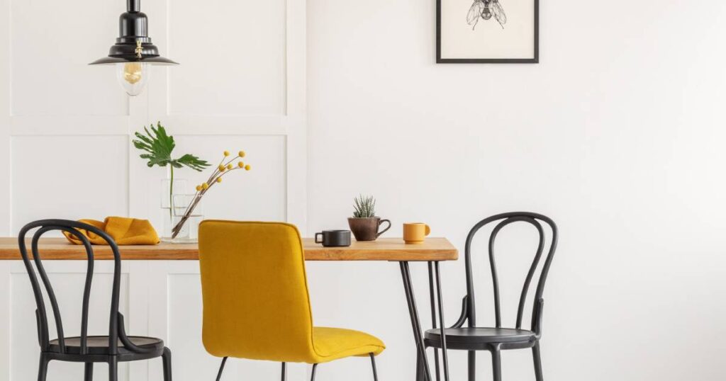 A bright kitchen with very white walls and table with a wood tabletop and three chairs accompanied by an overhead lamp.