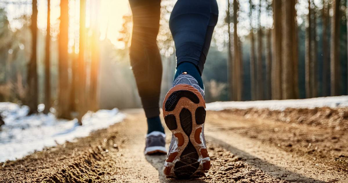 Low angle of a person's feet as they walk on a dirt path through a forest while the sun sets in the distance.