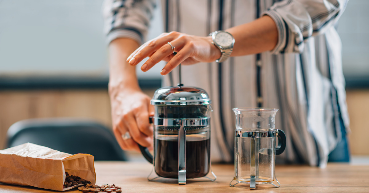 Someone at their kitchen island brewing coffee with a French press. They have a bag of coffee beans next to the press.